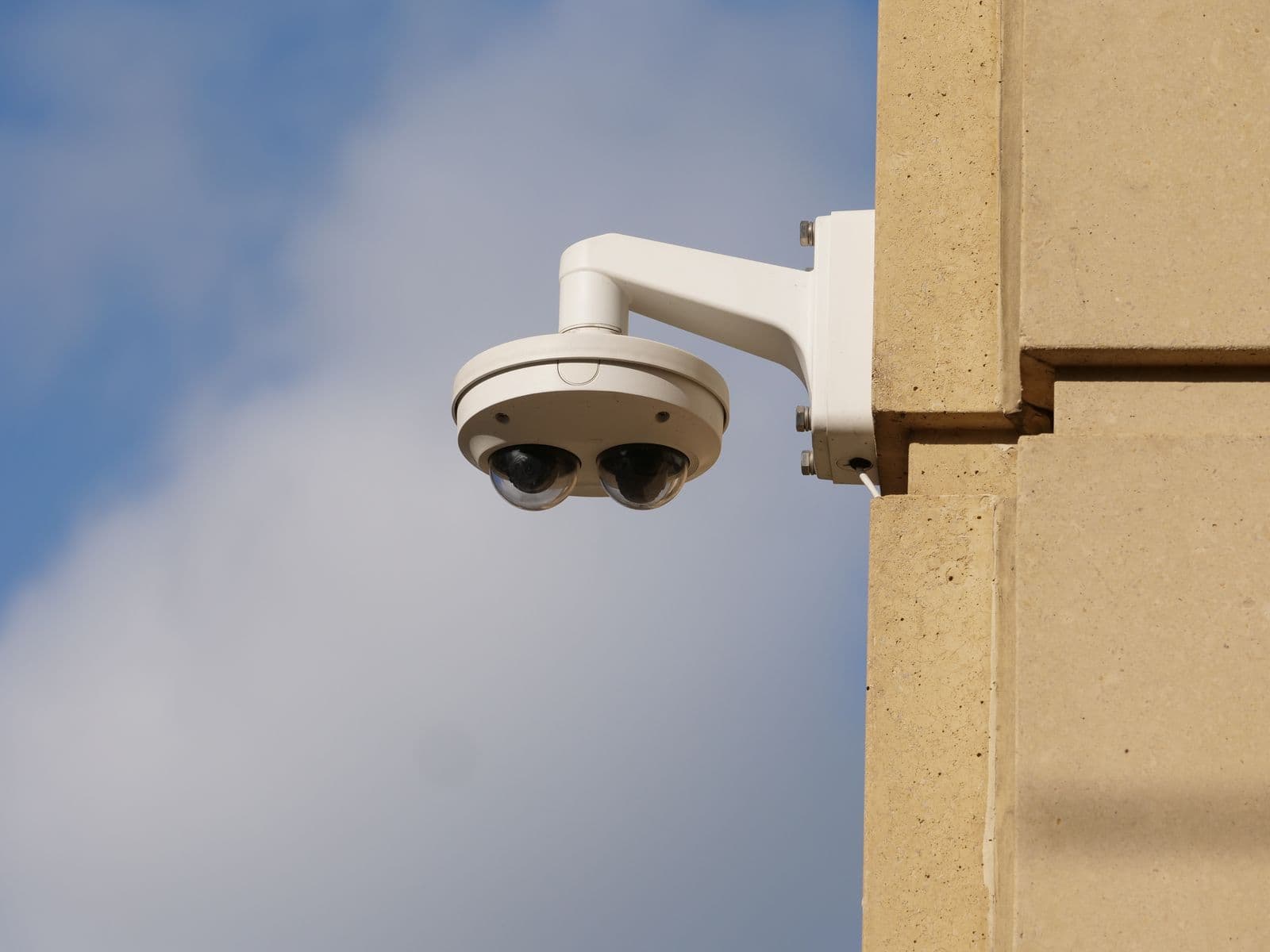 Caméra dôme blanche fixée sur une façade en pierre, sous un ciel bleu